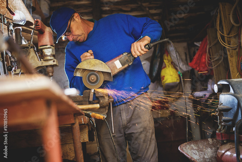 Craftsman sawing metal with disk grinder in workshop.
