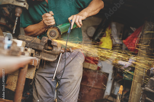 Craftsman sawing metal with disk grinder in workshop. Shallow depth of field.