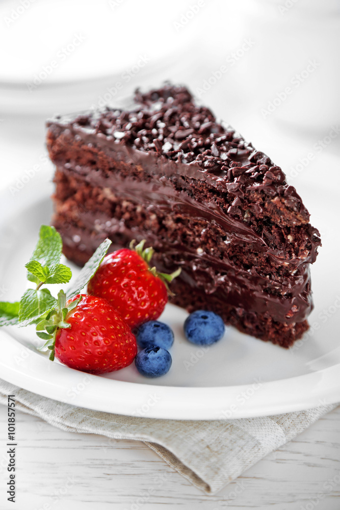 Chocolate cake with chocolate cream and fresh berries on plate, on light background Chocolate cake with chocolate cream and fresh berries on plate, on light background