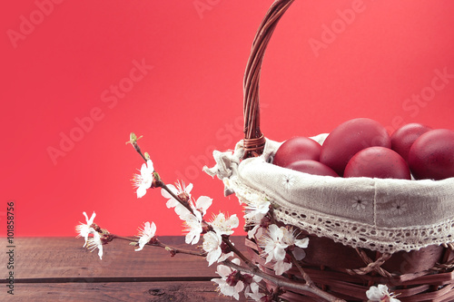 Basket with red easter eggs on rustic wooden table.