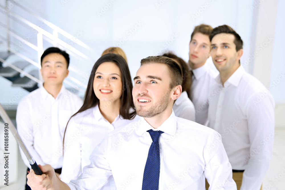 Young people using stick for group photo in office Young people using stick for group photo in office