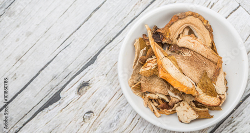 Dried porcini mushroom in a white bowl over wooden background