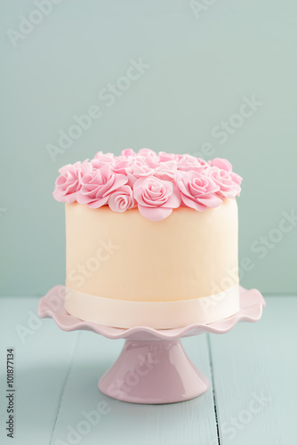 Ivory fondant covered cake with pink sugar roses on cake stand photo