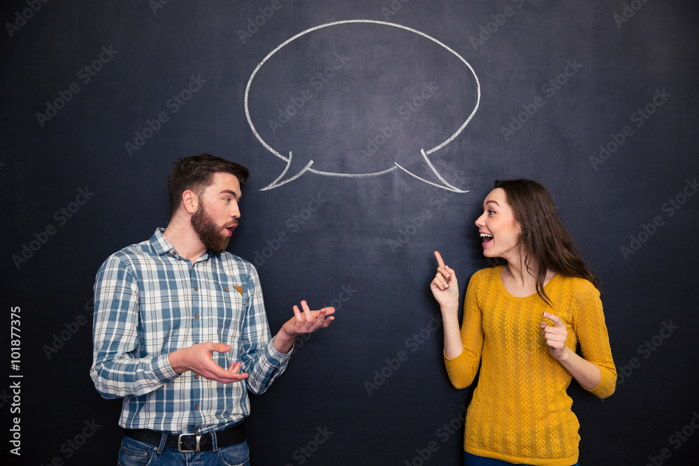 Beautiful couple talking over blackboard background with speech bubble