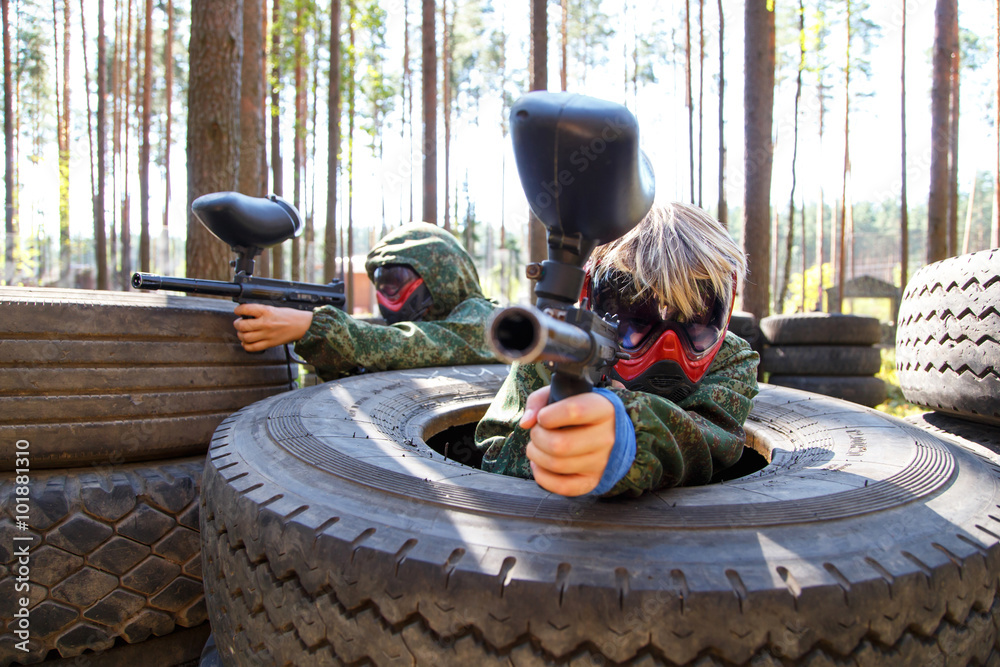 Φωτογραφία Two friends sitting in big truck tires with paintball guns