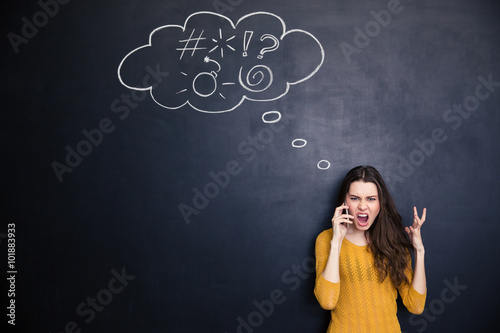 Crazy woman screaming on mobile phone standing over chalkboard background