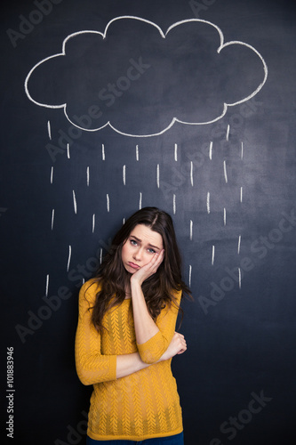 Sad woman standing under raincloud drawn above her on blackboard