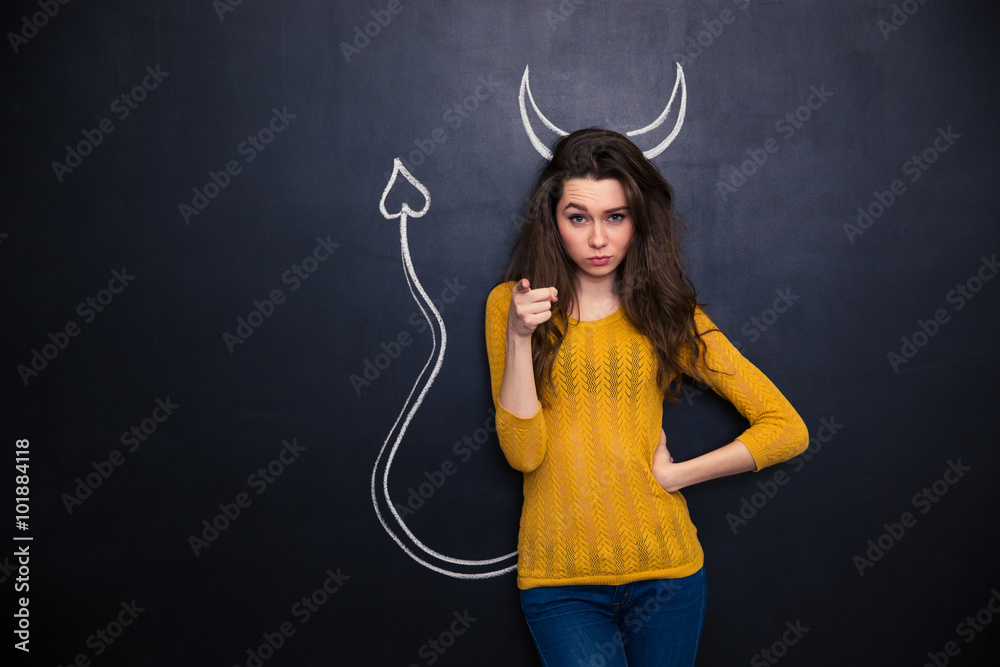 Attractive woman standing over blackboard background and pointing on you