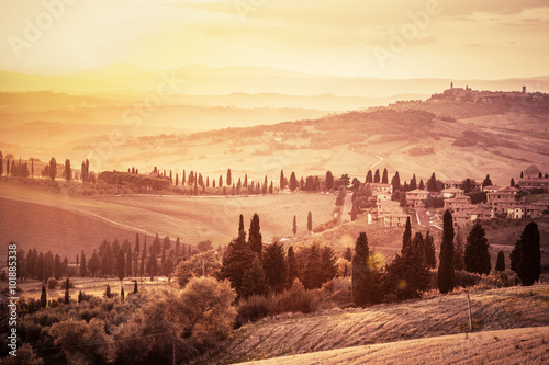 Wspaniały krajobraz Toskanii z drzewami cyprysowymi, gospodarstwami i małymi średniowiecznymi miasteczkami we Włoszech. Vintage zachód słońca