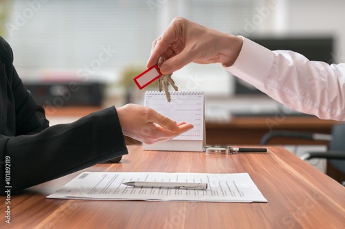 Real estate concept. Realtor is passing keys to the client sitting behind desk on blurred background.