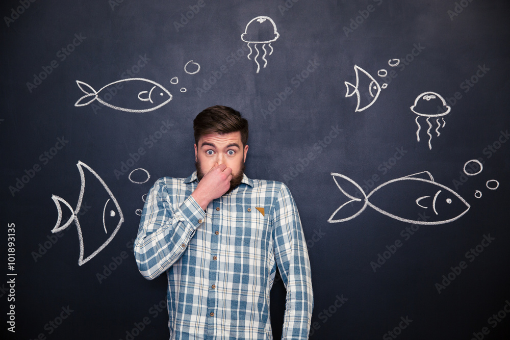 Amusing man closed nose and standing over chalkboard with fishes