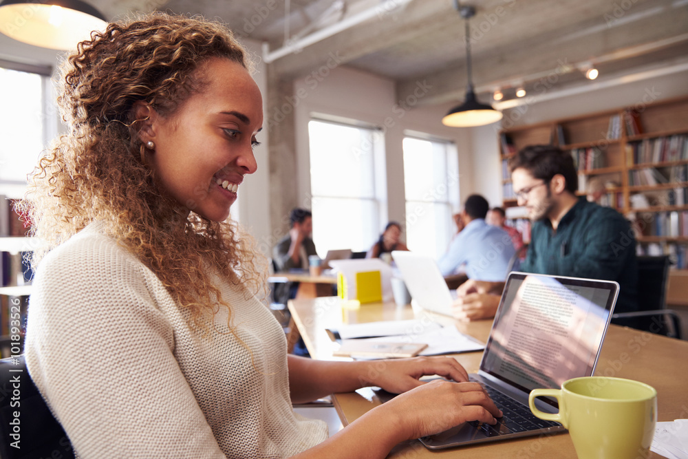 Businesswoman Using Laptop At Desk In Busy Office Businesswoman Using Laptop At Desk In Busy Office