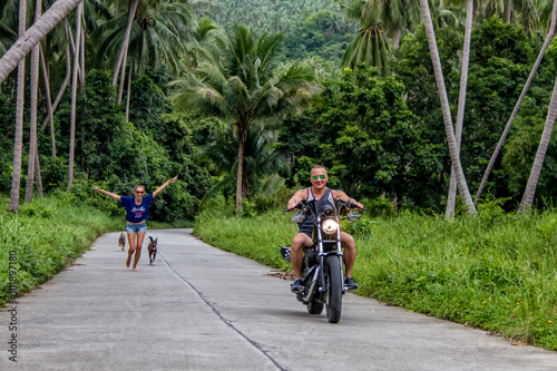 The guy on the bike rides through the jungle, followed by a woman and a dog runs