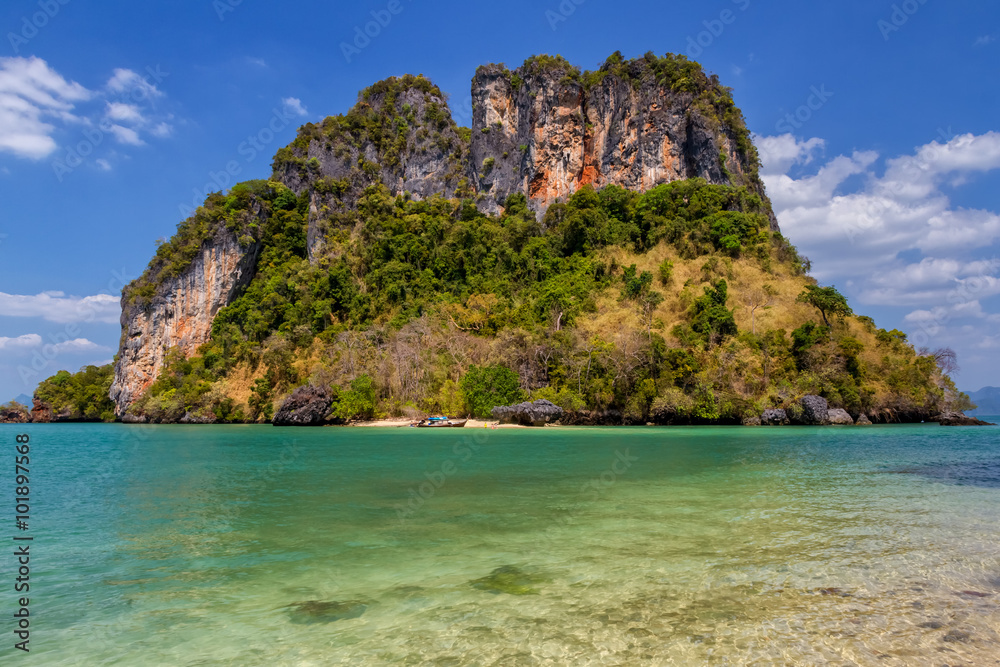 Small uninhabited tropical island with cliffs, trees, the sea around and blue sky Small uninhabited tropical island with cliffs, trees, the sea around and blue sky