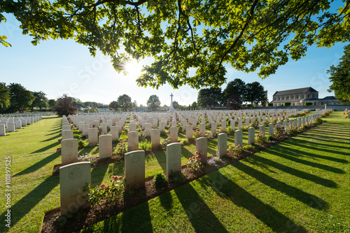 Les tombes d'un cimetière britannique à Ranville, Normandie, France au grand angle en contre-jour avec des branches d'arbres au premier plan. photo