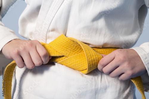 Hands tightening yellow belt on a teenage dressed in kimono