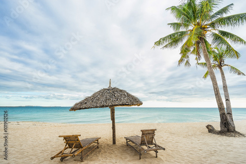 Two beach chairs, umbrella and Coconut palm on the beautiful island beach. Travel concept.