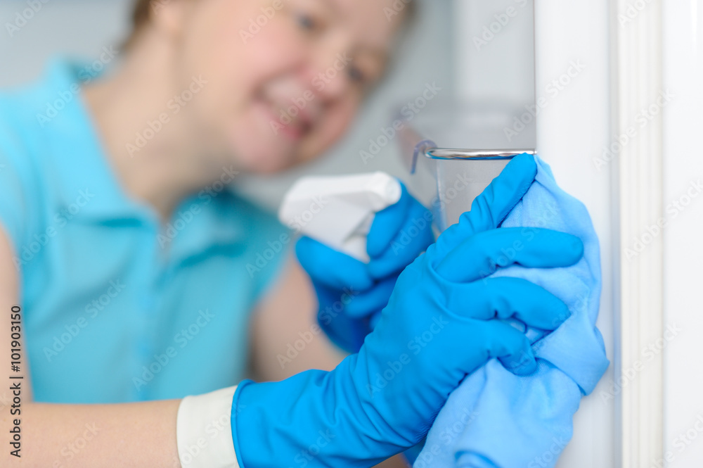 Beautiful smiling woman cleans the refrigerator with a rag and s