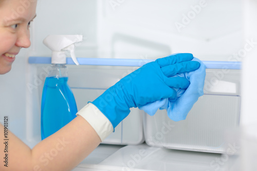 Smiling woman cleans the refrigerator with a rag and soapy liqui