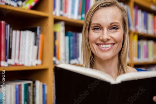 Happy female student reading a book in the library