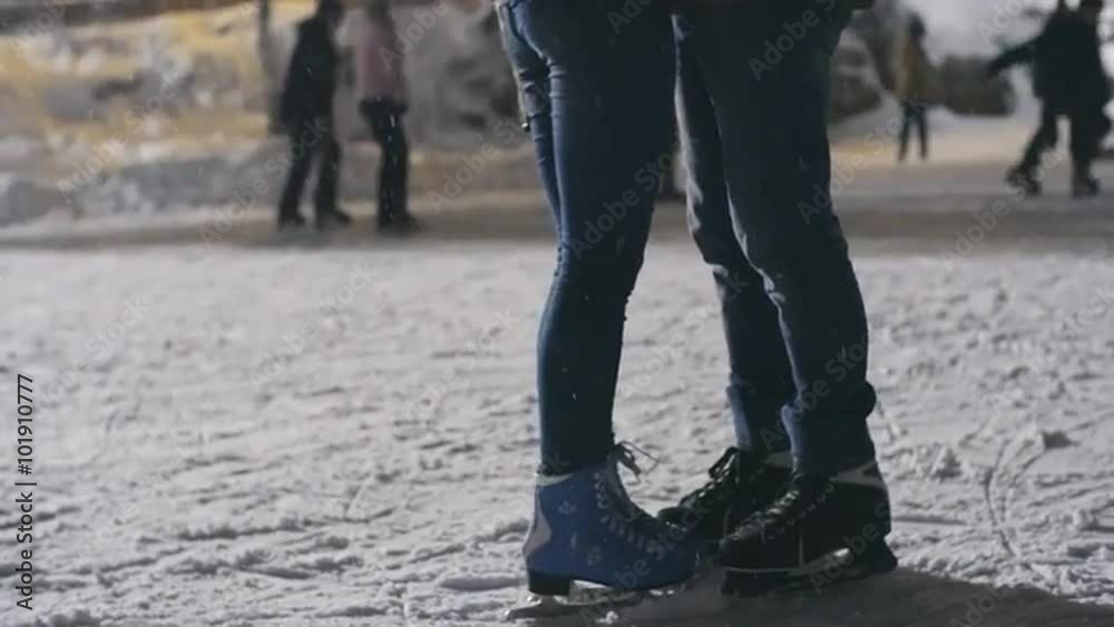 Low section of couple in ice skates hugging at outdoor skating rink, girl standing on tiptoes to kiss her boyfriend Low section of couple in ice skates hugging at outdoor skating rink, girl standing on tiptoes to kiss her boyfriend