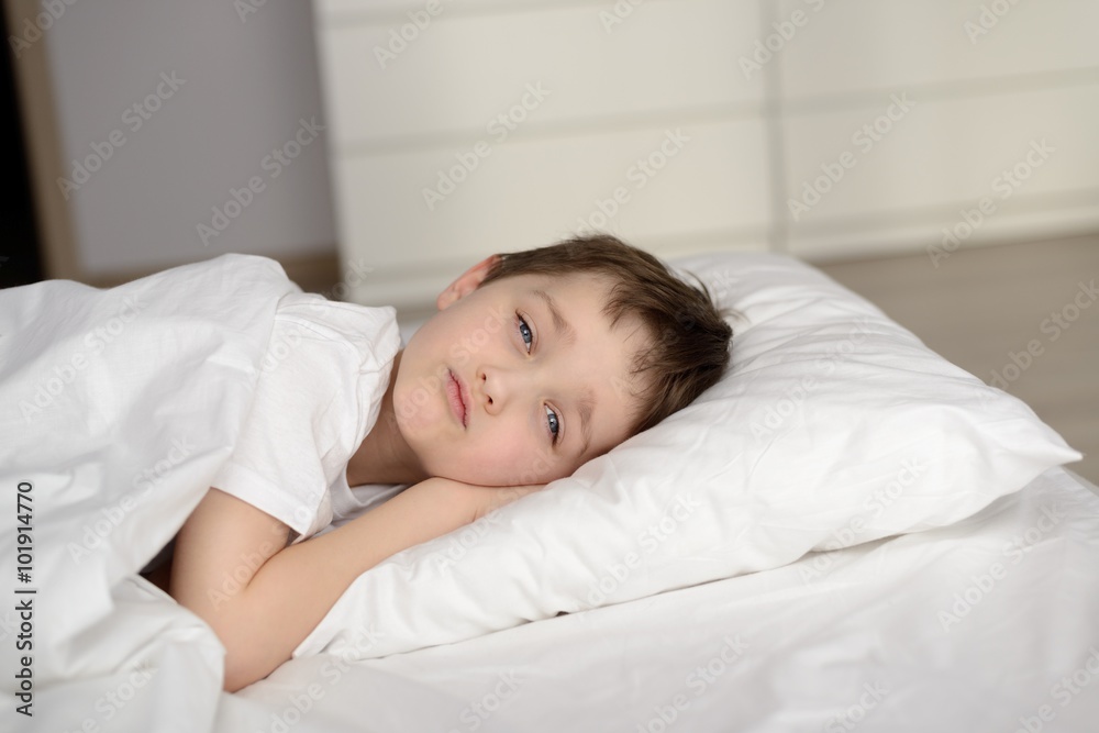 Little schoolboy resting in white bed with eyes open Little schoolboy resting in white bed with eyes open