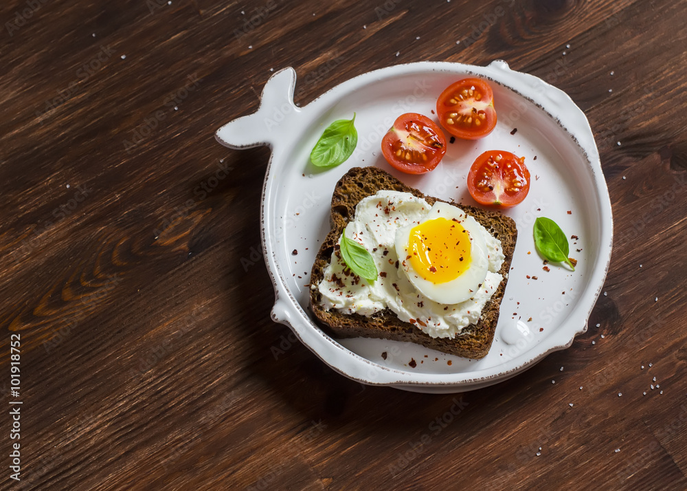 Open sandwich with feta cheese and boiled egg, tomatoes, and basil on a white plate on a wooden surface. Healthy breakfast or snack Open sandwich with feta cheese and boiled egg, tomatoes, and basil on a white plate on a wooden surface. Healthy breakfast or snack