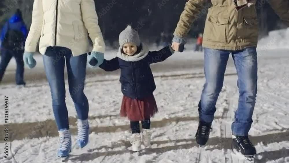 Adorable little girl enjoying ice skating with her parents at outdoor rink in park Adorable little girl enjoying ice skating with her parents at outdoor rink in park