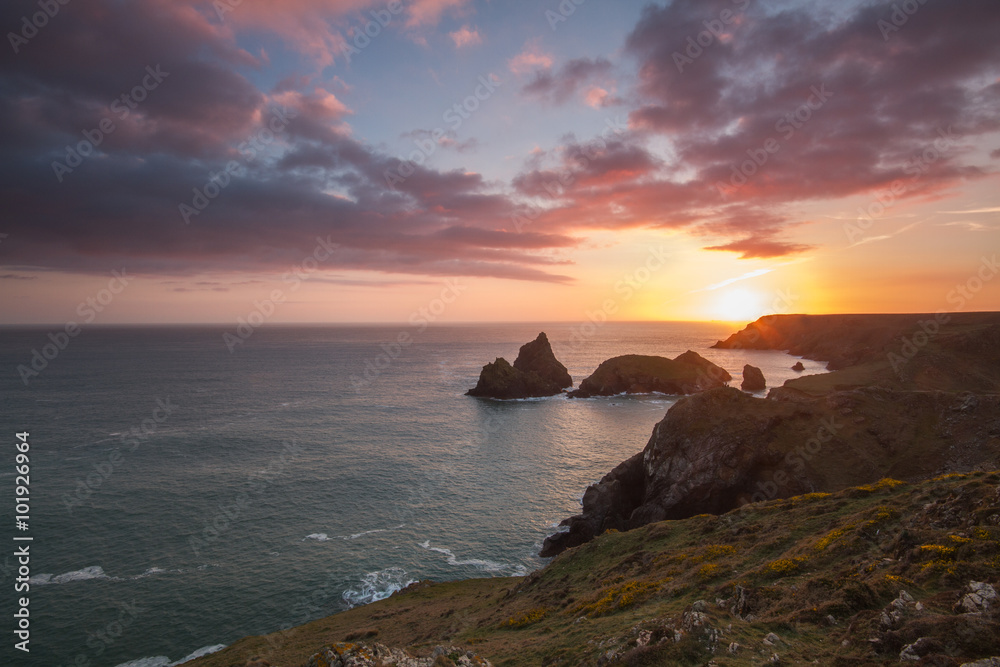 A rugged coastal sunset from a cliff top. The sun setting behind the ocean's horizon in Cornwall. A rugged coastal sunset from a cliff top. The sun setting behind the ocean's horizon in Cornwall.