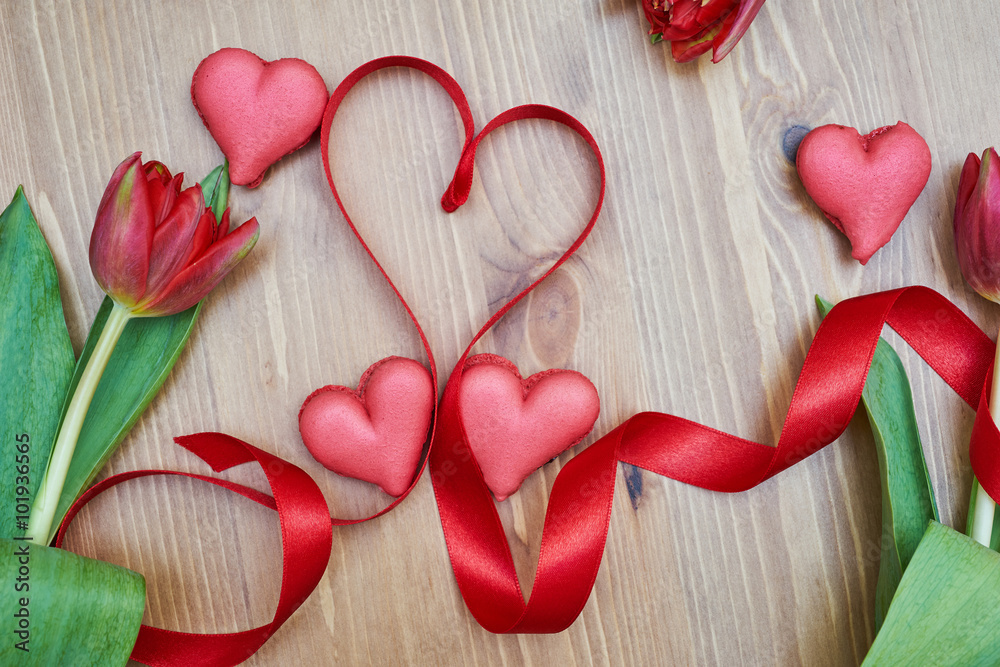 Fototapeta premium Heart-shaped macarons with flowers and ribbon on a wooden table. Creative decoration for Valentine's Day
