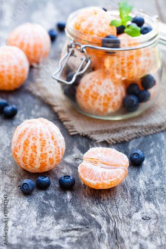 peeled tangerine or mandarin fruit and blueberry in glass jar on wooden table