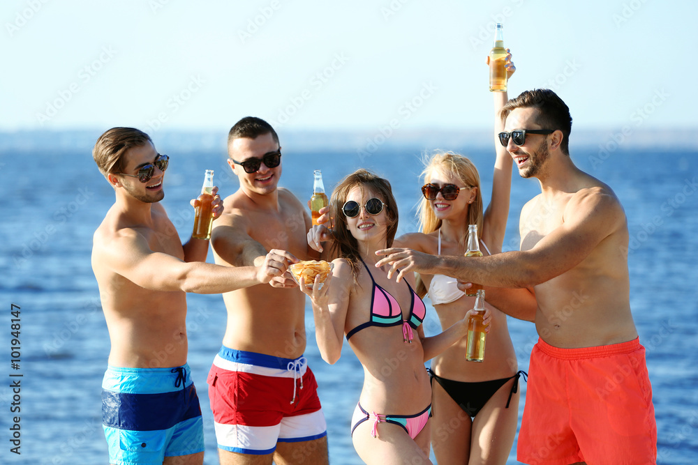 Happy young friends drinking beer at the beach, outdoors