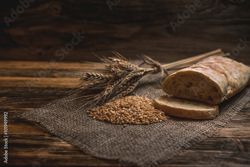 a ciabatta bread with wheat on stackcloth on a wooden rustic background photo