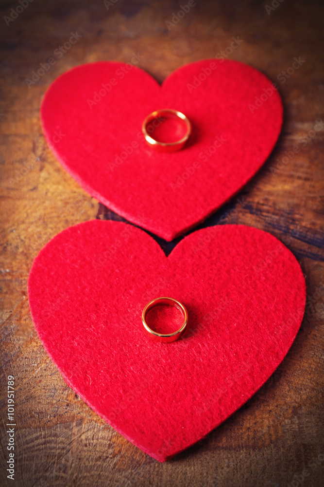 Fototapeta premium Two red felt hearts and wedding rings on wooden background closeup