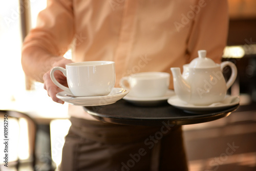 Waiter holding tray with teapot and cups close up