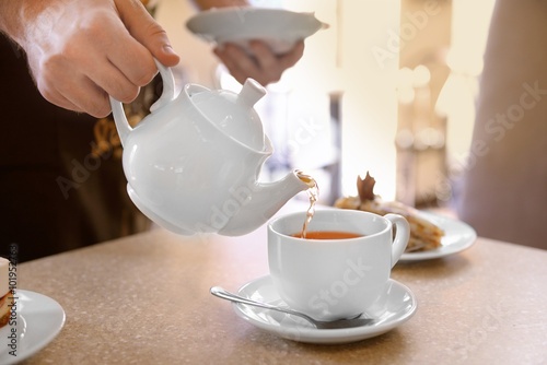 Waiter pouring tea into a white cup in cafe