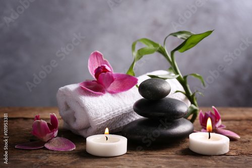 Spa stones with candles, purple orchid, bamboo and towel on wooden table against grey background