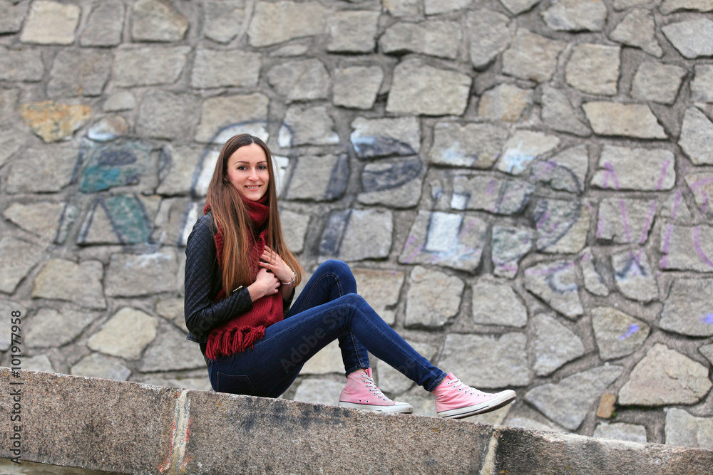 Beautiful brunette girl wearing leather jacket, blue jeans and pink sneakers Beautiful brunette girl wearing leather jacket, blue jeans and pink sneakers