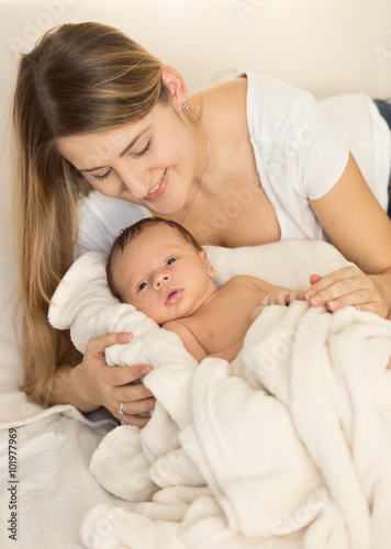 Toned portrait of caring mother hugging newborn baby on bed