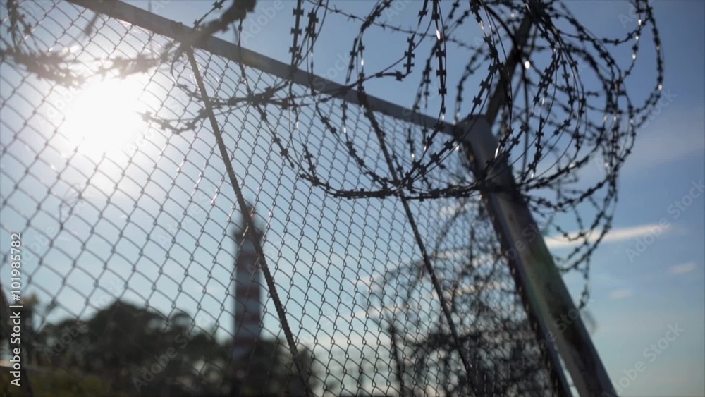 Barbed wire fence under sun focus in out. Summer. Jail. Lighthouse background Barbed wire fence under sun focus in out. Summer. Jail. Lighthouse background