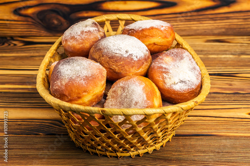 Homemade fresh donuts sprinkled with powdered sugar in wicker basket on wooden table