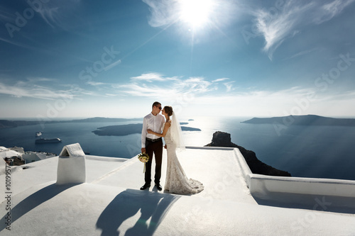 Handsome happy groom and bride in white dress holding hands sea and islands background