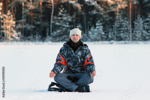 yogi young man practices yoga and meditates on the snow in the winter
