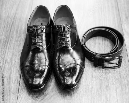 New black man shoes and black belt on wooden brown surface of floor. Black and white picture of male stylish accessories for solemn events.