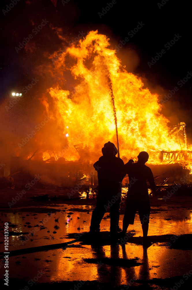 Fototapeta premium Silhouette of Firemen fighting a raging fire with huge flames of burning timber