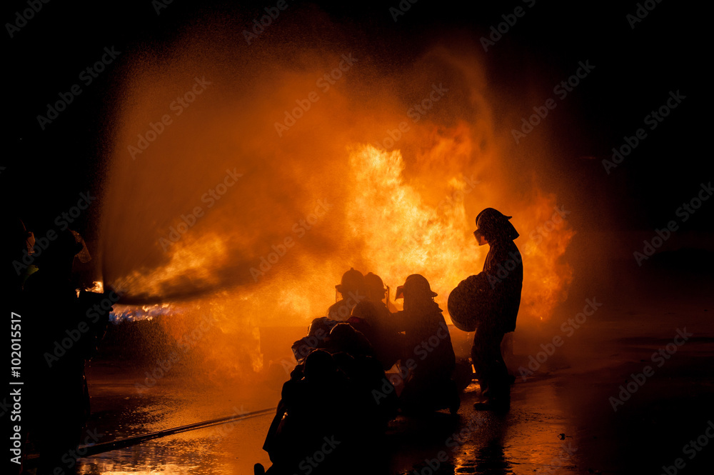 Fototapeta premium Silhouette of Firemen fighting a raging fire with huge flames of burning timber