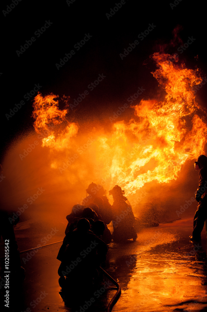 Fototapeta premium Silhouette of Firemen fighting a raging fire with huge flames of burning timber