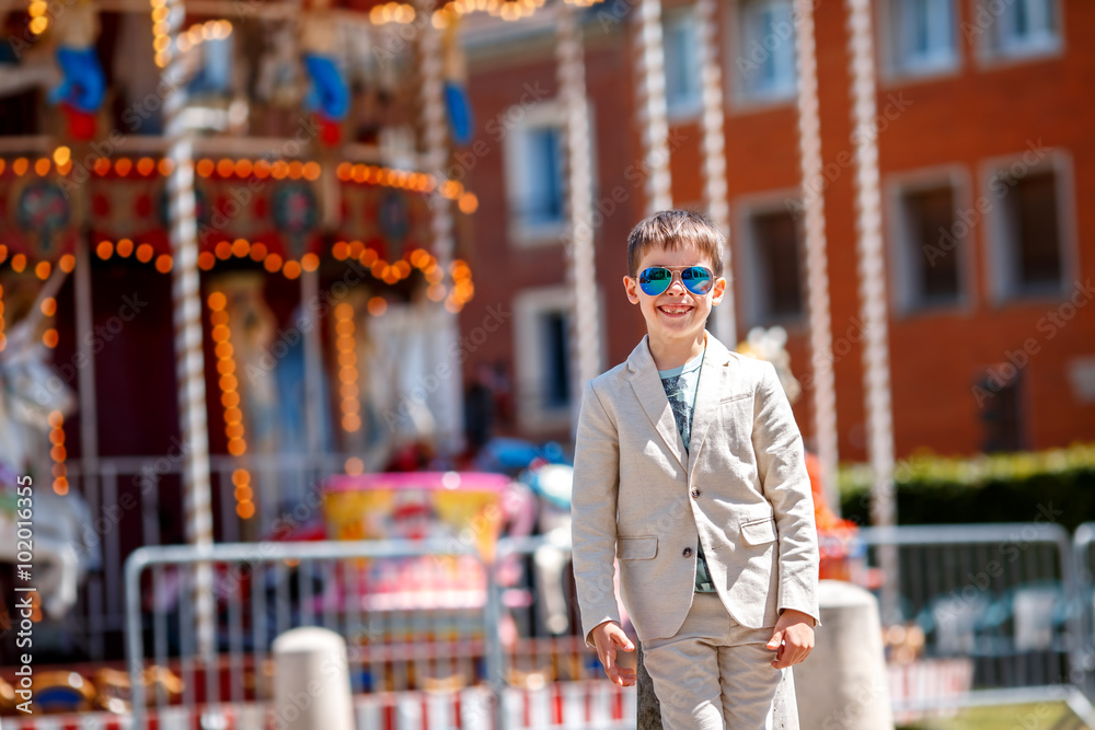Stylish kid in a nice suit and glasses near the traditional French merry-go-round