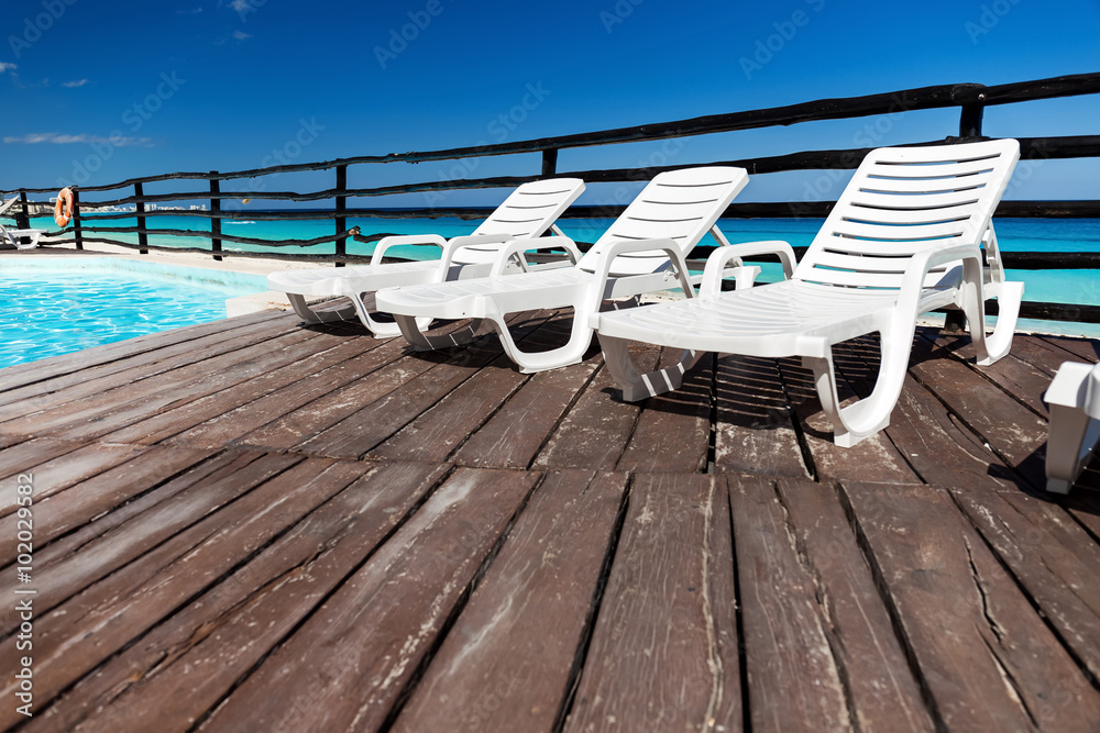 Luxury sunbeds on wooden floor near swimming pool