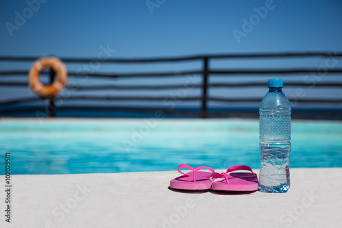Plastic bottle with pure water and slippers near swimming pool